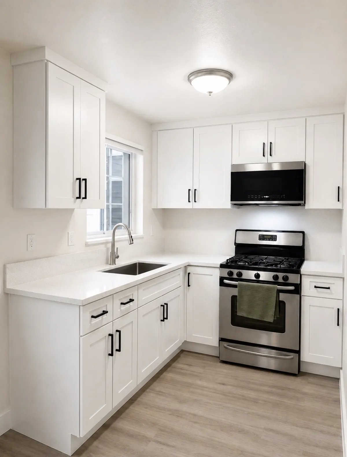 The same kitchen completed — white shaker cabinetry, matte black hardware, quartz counters and stainless appliances, by Serrano Construction